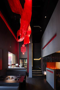 Modern bar area with black and red decor, bottles, and a refrigerator, creating an inviting atmosphere for socializing