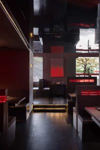 A modern restaurant dining area with multiple tables and chairs, red walls, and warm lighting