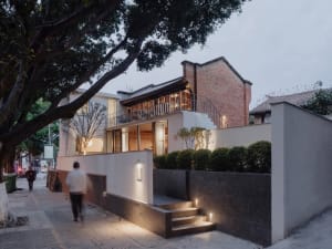 A modern house with a large white wall, a black staircase, and a brick exterior, set in a calm and serene environment