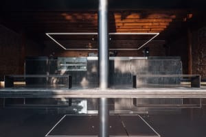 Modern bar interior with a black countertop, brick wall, and metal pole, featuring benches and a sophisticated atmosphere