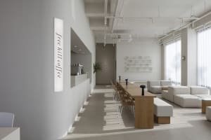 Open living area with white walls and floors, featuring chairs, a dining table, a potted plant, and decorative vases