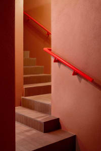 Orange hallway with red handrails, concrete walls, and a staircase leading upwards