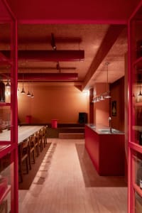 Warm and inviting kitchen area with a dining table, chairs, and red walls, surrounded by scattered bottles and natural light
