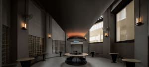 Open living space with a circular table, dining tables, chairs, and a fireplace, surrounded by tile-adorned walls