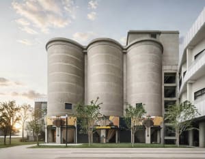 A large building with a modern industrial feel, featuring a circular structure, concrete appearance, and ample natural light from multiple windows