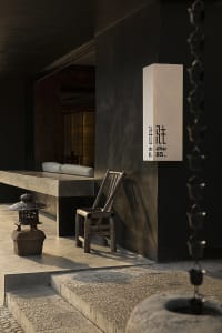 Modern interior space with a black wall, stone bench, and two chairs, featuring a vase and clean lines