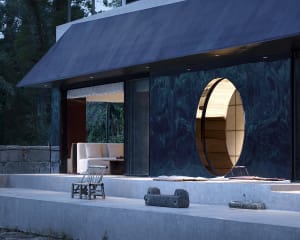 A modern house with a circular doorway made of wood, surrounded by a patio and featuring a cozy seating area inside
