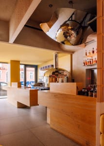 Warm and inviting restaurant interior with a wooden bar counter, large oven, and rustic design elements