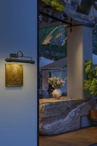 A warm and inviting cafe space with a stone countertop, potted plants, and a vase of flowers, set up for outdoor seating with multiple umbrellas