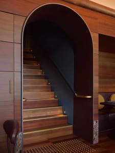 A dark interior staircase with a wooden structure and black railing, flanked by two chairs near the bottom, creating a mysterious atmosphere