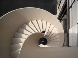 A spiral staircase in a well-lit building with concrete steps, suggesting a sense of depth and intrigue