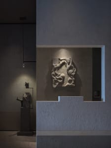 A modern art gallery featuring a stone sculpture on a wall, surrounded by a neutral background, with a warm and inviting atmosphere