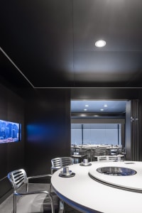 A modern restaurant dining area with multiple tables and chairs, surrounded by windows allowing natural light to enter the space