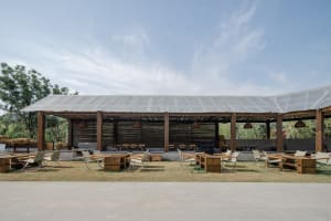 Outdoor dining space with tables, chairs, and umbrellas under a large roof structure