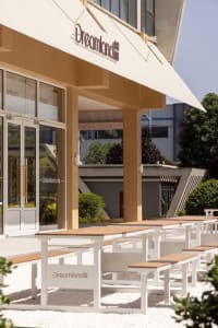 Architectural rendering of a modern building with a wooden facade, metal roof, and multiple windows, surrounded by outdoor benches