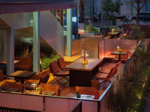 A nighttime outdoor restaurant scene with multiple tables and chairs, potted plants, and a warm ambiance