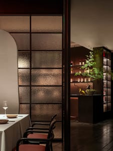 Sophisticated restaurant interior with a dining table, chairs, and a kitchen in the background, featuring wooden accents and wine bottles