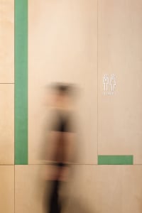 A man walks down a green-walled office hallway with white walls on the opposite side, featuring two signs and a professional atmosphere