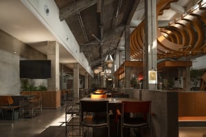 A modern restaurant interior with a large dining area featuring multiple tables and chairs, well-lit for a comfortable atmosphere