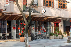 A modern Asian restaurant with a dining area, potted plants, and red lanterns outside, creating a comfortable and inviting atmosphere