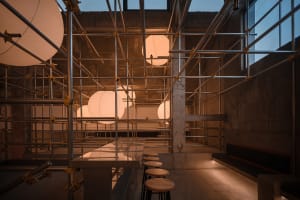 Industrial restaurant space with concrete walls, multiple dining tables, and dim lighting