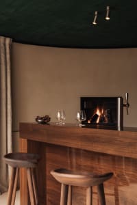 Cozy living space with a wooden bar counter, wine glasses, and a chair, featuring warm and inviting atmosphere
