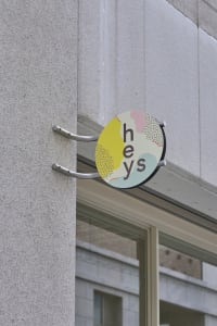 A concrete building exterior with a yellow sign featuring white letters that spell out Hey's