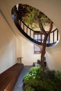 A modern spiral staircase with a wooden structure and black railing, set in a well-lit living area with a bench at the base