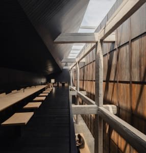 A spacious dining hall with wooden floors, tables, and a sophisticated atmosphere, featuring elegant lighting and warm wooden elements