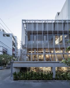 A modern building with multiple levels, featuring a mix of concrete, glass, and wood materials, with chairs and a contemporary design