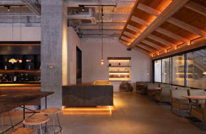 Open modern living space with a grey countertop island, concrete walls, wooden elements, chairs, and a dining table, with a bright and inviting atmosphere