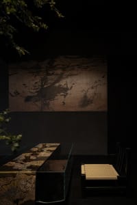 Dark dining space with a glass table, chairs, and various items, surrounded by a larger living area with a couch