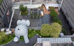 A lively art gallery with a large foam elephant sculpture as the centerpiece, surrounded by smaller elephants and people enjoying the display