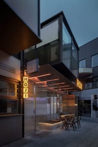 A modern building exterior at night with a large glass front, various window sizes and shapes, and artificial lighting creating a warm glow