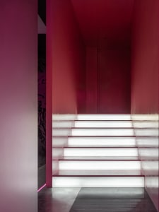 A grand staircase in a museum setting with marble steps, a red wall, and a sense of elegance