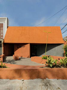 A welcoming orange building with a red roof, featuring two benches and a chair in a comfortable outdoor setting