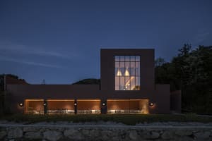 A modern building at night with a large window, stone and glass elements, and several chairs in a dining area or waiting lounge