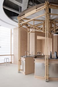 A kitchen area with a sink under a wooden structure, two bottles near the sink, and a functional yet stylish atmosphere
