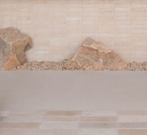 A serene outdoor space with a rock wall, stone walkway, and three large boulders creating a unique design element