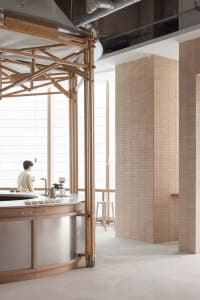 A restaurant interior with a wooden theme, featuring a metal countertop, sink, and coffee maker, with two people in the scene