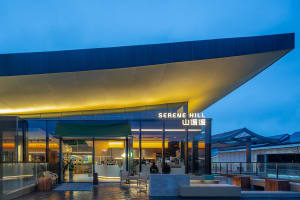 A modern building with a glass and steel exterior, featuring a yellow roof, and chairs outside, set against a night sky