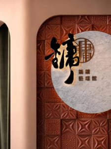 A well-lit Asian restaurant interior with a wall featuring Chinese characters and a tile pattern, creating a warm atmosphere
