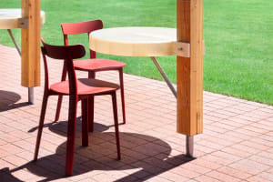 An inviting outdoor patio with two red chairs and two dining tables on a brick surface, perfect for al fresco dining or conversations