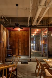 Rustic restaurant interior with wooden walls and floors, dining area, kitchen, and potted plants, creating a warm and inviting atmosphere