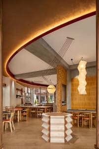 Modern restaurant interior with wood accents, concrete, and metal, featuring a dining area, bar, and warm lighting
