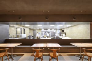 Industrial kitchen dining area with wooden tables, chairs, appliances, and natural light from a window
