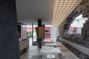 Modern restaurant interior with a dining area, bar, and seating options, featuring concrete and wood materials and warm overhead lighting