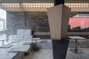 A modern restaurant interior with a large wooden sculpture, grey stone walls, and a black and white theme, featuring tables and chairs in a stylish and inviting atmosphere