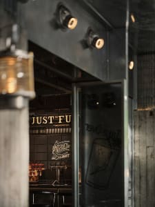 A cozy bar with a wooden counter and numerous bottles on display, illuminated by several lights