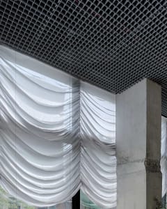 A modern industrial space with a concrete wall, metal beam, and curtains, featuring a sleek and contemporary atmosphere